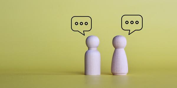 2 wooden figures, each with a speech bubble above them. 2 wooden figures, each with a speech bubble above them.