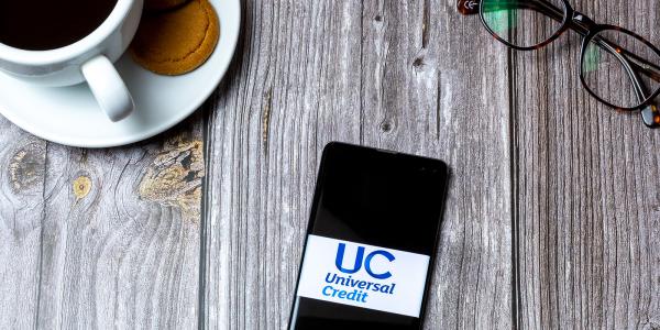 A table with a hot beverage and a mobile phone showing 'UNIVERSAL CREDIT' on the screen. A table with a hot beverage and a mobile phone showing 'UNIVERSAL CREDIT' on the screen.
