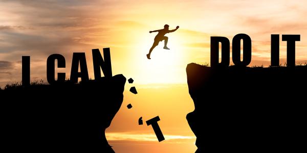 A person jumping from one cliff edge to another, the words 'I CAN DO IT' can be seen across the cliffs. The jump has knocked the 'T' from 'CAN'T'. A person jumping from one cliff edge to another, the words 'I CAN DO IT' can be seen across the cliffs. The jump has knocked the 'T' from 'CAN'T'.