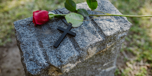 A gravestone with a black cross and a red rose laid on top A gravestone with a black cross and a red rose laid on top