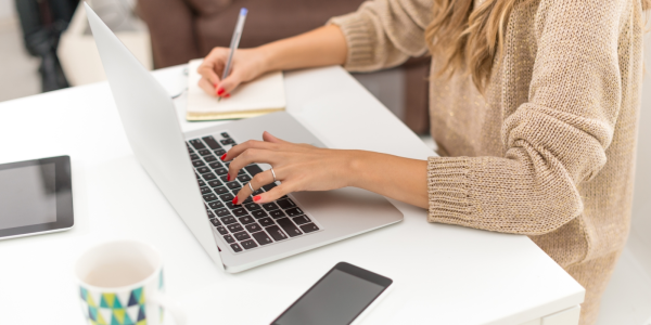 A person working on a laptop with a pen and paper to hand. A person working on a laptop with a pen and paper to hand.