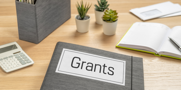 A desk with a folder on top, the folder is named 'GRANTS'. A desk with a folder on top, the folder is named 'GRANTS'.