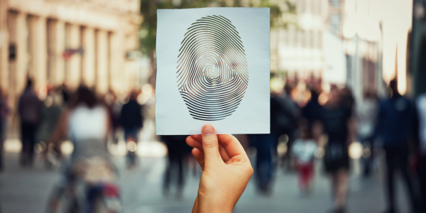A person holding up an mage of a fingerprint, in the background city streets filled with people can be seen. A person holding up an mage of a fingerprint, in the background city streets filled with people can be seen.