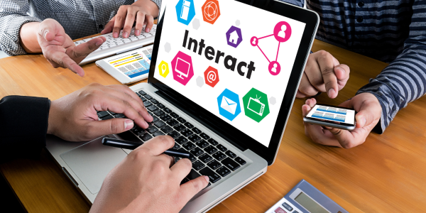 A group of people sitting around a laptop that has the word 'INTERACT' on the screen. A group of people sitting around a laptop that has the word 'INTERACT' on the screen.