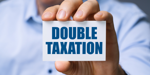 Person holding up a card with the words 'DOUBLE TAXATION' on it in blue text. Person holding up a card with the words 'DOUBLE TAXATION' on it in blue text.