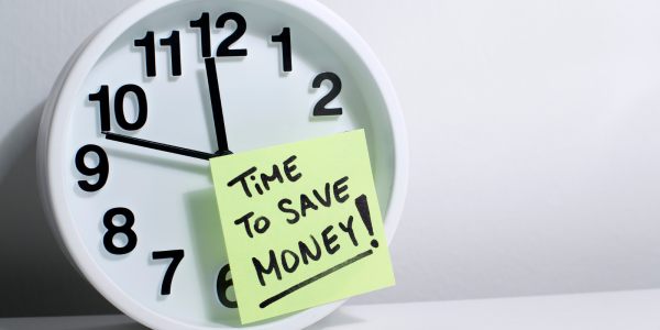 A wall clock with a post it note stuck to the front, the note reads 'TIME TO SAVE MONEY!' A wall clock with a post it note stuck to the front, the note reads 'TIME TO SAVE MONEY!'