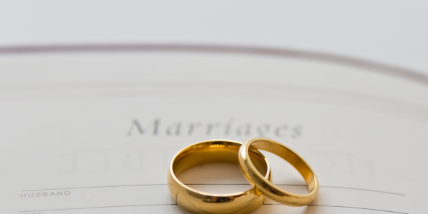 2 wedding bands sat on top of a paper with the word 'Marriages' written at the top. 2 wedding bands sat on top of a paper with the word 'Marriages' written at the top.