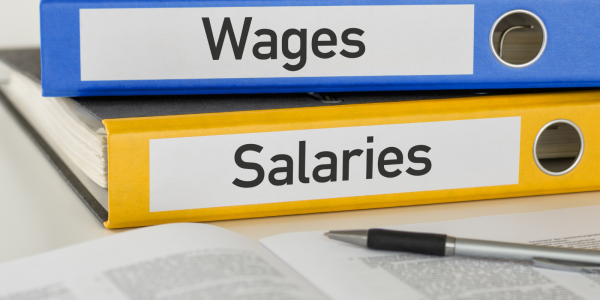 Two folders sat on a desk one says 'WAGES' and the other 'SALARIES' Two folders sat on a desk one says 'WAGES' and the other 'SALARIES'