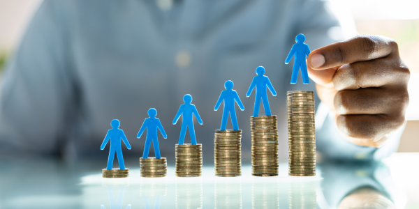 6 piles of coins gradually getting larger from left to right each with a small plastic person figure on top. 6 piles of coins gradually getting larger from left to right each with a small plastic person figure on top.