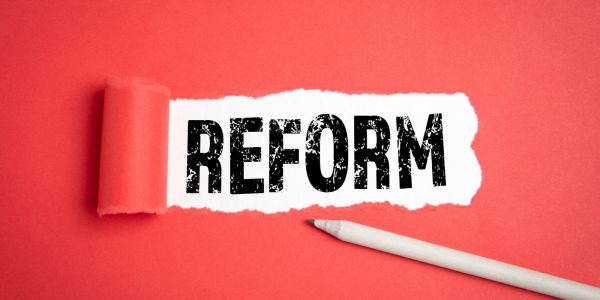 A red paper with a tear in the centre, through the tear the word 'REFORM' can be seen in bold black text A red paper with a tear in the centre, through the tear the word 'REFORM' can be seen in bold black text