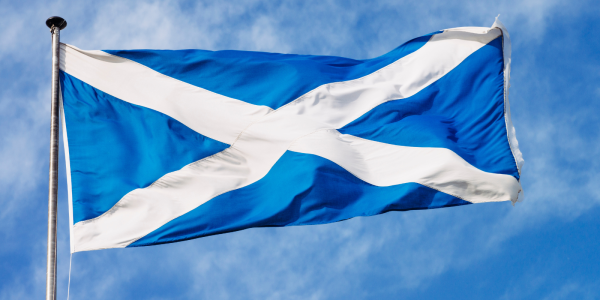 Scottish flag blowing in the wind against a blue sky background. Scottish flag blowing in the wind against a blue sky background.