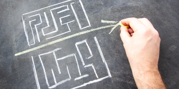 two hand drawn mazes on a chalkboard, and a person drawing a straight arrow through the gap between the two. two hand drawn mazes on a chalkboard, and a person drawing a straight arrow through the gap between the two.