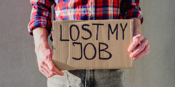 A person holding a piece of cardboard with the words 'LOST MY JOB' written on it in black ink A person holding a piece of cardboard with the words 'LOST MY JOB' written on it in black ink