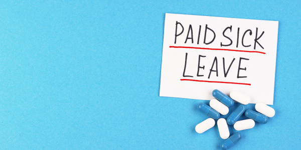 A bunch of blue and white pills and a sign saying 'PAID SICK LEAVE' A bunch of blue and white pills and a sign saying 'PAID SICK LEAVE'