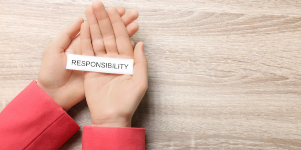 A person holding a small piece of white paper with the word 'RESPONSIBILITY' on it in black text. A person holding a small piece of white paper with the word 'RESPONSIBILITY' on it in black text.