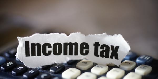 A torn piece of paper with the words 'INCOME TAX' typed on it, the paper is sat on a calculator. A torn piece of paper with the words 'INCOME TAX' typed on it, the paper is sat on a calculator.