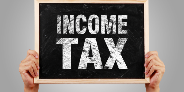 A person holding up a small chalkboard with the words 'INCOME TAX' written on it in white chalk. A person holding up a small chalkboard with the words 'INCOME TAX' written on it in white chalk.