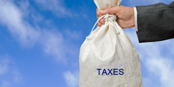 A person holding a white sack, the sack has the word 'TAXES' printed on it in blue text. A person holding a white sack, the sack has the word 'TAXES' printed on it in blue text.