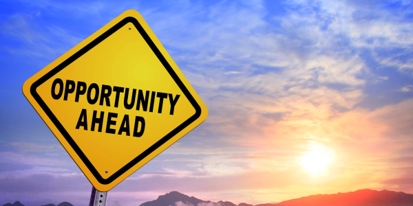 A yellow road sign with the words 'OPPORTUNITY AHEAD' in black text, a sunset can be seen in the background A yellow road sign with the words 'OPPORTUNITY AHEAD' in black text, a sunset can be seen in the background