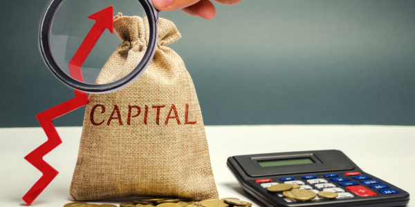 A brown sack with the word 'CAPITAL' on it, a calculator, a red arrow pointing upwards and a magnifying glass. A brown sack with the word 'CAPITAL' on it, a calculator, a red arrow pointing upwards and a magnifying glass.