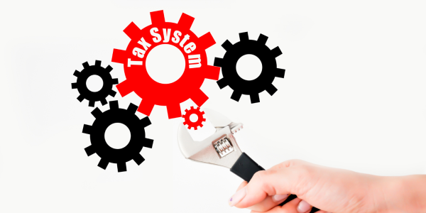 various sized cogs interlinked together, the largest red cog has the words 'TAX SYSTEM' on it, a person is turning the smallest red cog with an adjustable wrench. various sized cogs interlinked together, the largest red cog has the words 'TAX SYSTEM' on it, a person is turning the smallest red cog with an adjustable wrench.