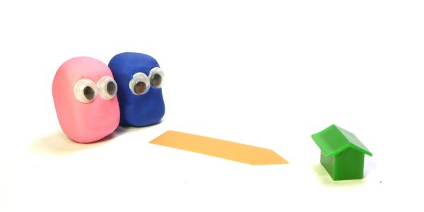 2 people made from play-doh with googly eyes (one pink, one blue), following an arrow marked on the floor towards a tiny green house. 