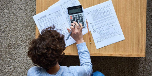 A person sat at a desk with papers and a calculator. A person sat at a desk with papers and a calculator.