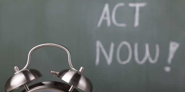 A bedside alarm clock sat in front of a chalk board, the board reads 'ACT NOW!' A bedside alarm clock sat in front of a chalk board, the board reads 'ACT NOW!'