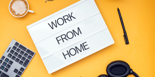 A yellow background with a keyboard, headphones, hot beverage, pen and a paper that reads 'WORK FROM HOME' A yellow background with a keyboard, headphones, hot beverage, pen and a paper that reads 'WORK FROM HOME'