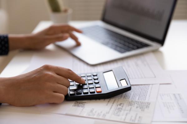 Close up of young female electronic bank client using calculator in paperwork with accounts bills before providing payment online by laptop Close up of young female electronic bank client using calculator in paperwork with accounts bills before providing payment online by laptop