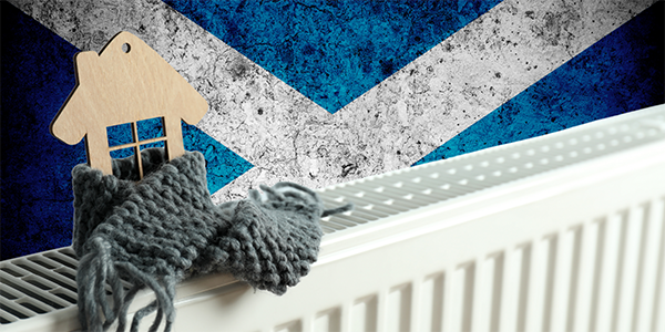 A white metal radiator with a wooden house on top wrapped in a scarf, behind the Scottish flag can be seen. 