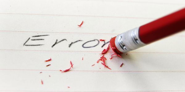 The word 'ERROR' written on a piece of lined paper is being rubbed out. 