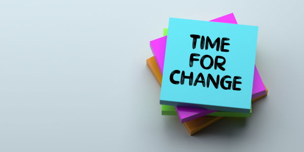 A pile of various coloured blocks of sticky notes, the top note has writing on it that reads 'TIME FOR CHANGE' 