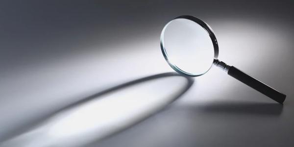 A magnifying glass stood on its side, showing the objects shadow against a grey background