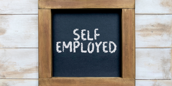 A wooden photo frame with a chalk board inside, on the chalk board the words 'SELF EMPLOYED' can be seen.