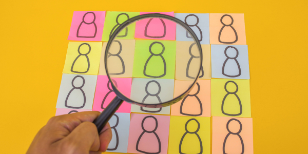people drawn on coloured pieces of paper, someone is looking at them closely with a magnifying glass. 
