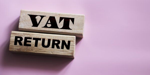 Wooden blocks containing the words 'VAT RETURN' on them against a pale pink background