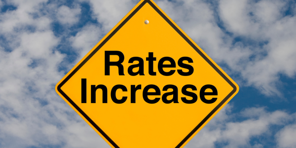 A yellow diamond shaped sign with the words 'RATES INCREASE' in black text against a cloudy blue sky