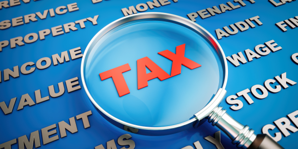 A magnifying glass hovering over the word 'TAX' against a blue background filled with different words. 