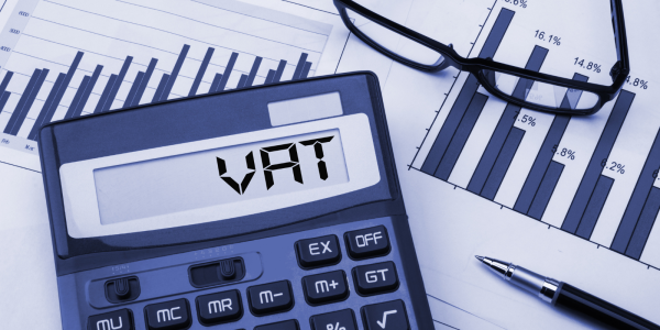 Papers on a desk with glasses and a calculator that reads the word 'VAT' 