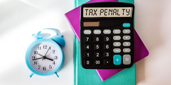 Calculator displaying ‘Tax Penalty’ beside a blue alarm clock and colourful notebooks.