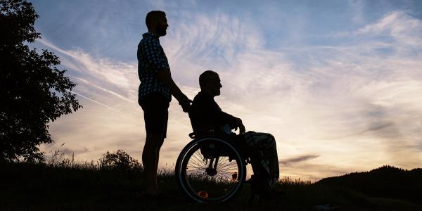 Image of the silhouette of a man pushing another man in a wheelchair