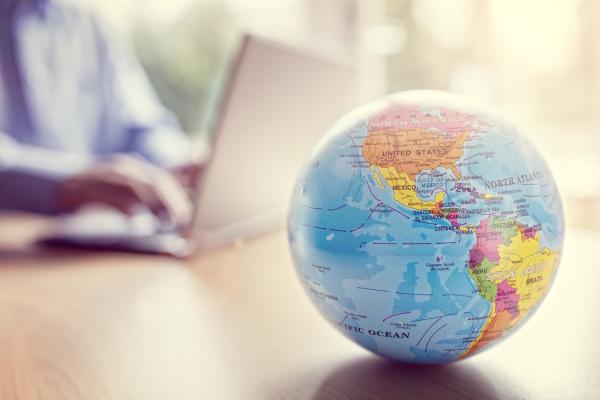 Person typing an a laptop with a globe in the foreground. ©istock/BrianAJackson