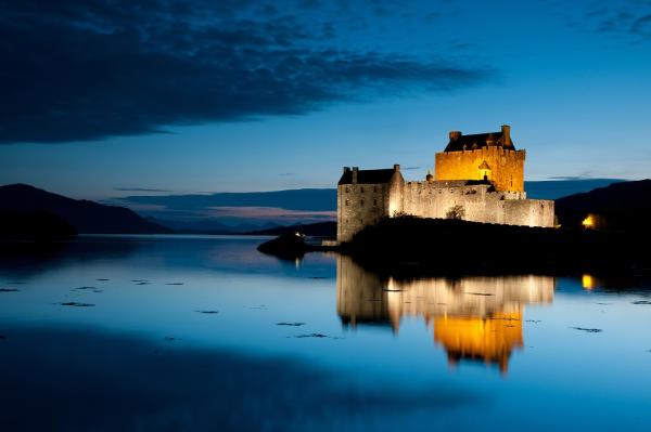 Walled building lit up at night, next to a lake.